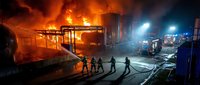 Firefighters battle massive warehouse blaze with emergency vehicles and dramatic flames illuminating night scene for disaster response training materials.
