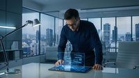 Businessman in dark blue shirt and glasses working with holographic digital interface on tablet at modern office desk with city skyline view.