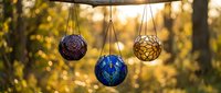 Colorful handcrafted woven spheres hanging outdoors with warm golden sunset bokeh background creating peaceful garden decoration atmosphere.