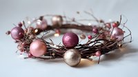 Festive wreath with pink, burgundy, and champagne ornaments intertwined with delicate twigs and berries on white background. Perfect for holiday decor.