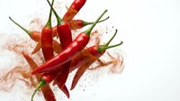 Red chili peppers with paprika powder explosion on white background, spicy hot seasoning ingredient for cooking and culinary arts isolated.