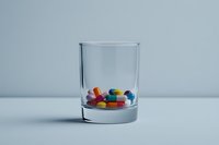 Colorful pills and capsules inside a clear glass on a light blue background, symbolizing medication, healthcare, and addiction concepts.