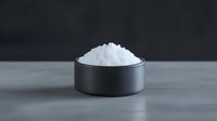 White sea salt crystals in black ceramic bowl on gray concrete surface against dark background, minimalist food photography composition.