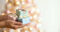 Hands holding small wrapped gift boxes with ribbons against warm bokeh lights background for holiday celebrations and special occasions.