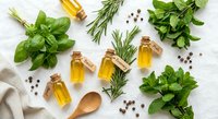 Fresh herbs basil rosemary mint with essential oil bottles and peppercorns on white wooden background for natural cooking and aromatherapy wellness.