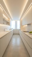 Modern minimalist galley kitchen with white cabinetry, integrated appliances, and linear ceiling lights creating a bright, contemporary cooking space for interior design and home renovation projects.