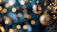 Elegant gold and silver Christmas ornaments hanging on pine branches with soft bokeh lights creating magical holiday atmosphere. Perfect for seasonal designs.
