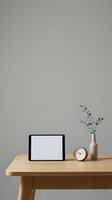 Minimalist workspace with blank tablet, wooden clock and eucalyptus branch in vase on natural wood desk against neutral gray wall for modern office design.