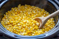 Fresh corn kernels cooking in slow cooker with wooden spoon, healthy vegetable side dish preparation for family meals and holiday gatherings.