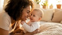 Happy African American mother bonding with adorable baby in cozy living room with warm natural light creating intimate family moment at home.