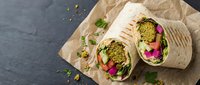 Vegan wraps filled with green pesto, fresh vegetables and sprouts on kraft paper, overhead view for healthy eating and meal prep content.
