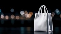 White shopping bag with handles against blurred city lights bokeh background for retail marketing and consumer lifestyle concepts.