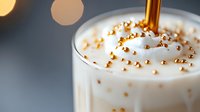 Creamy milkshake topped with golden sprinkles and metallic straw against blurred background, macro shot capturing luxurious texture and festive drink presentation.