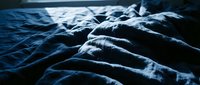 Crumpled blue fabric with deep folds and shadows, creating texture and depth. Suitable for backgrounds, textile design, and abstract compositions.