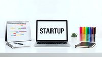 Startup concept with laptop on white desk, calendar, colorful markers, notebook, and small plant for business and entrepreneurship themes.