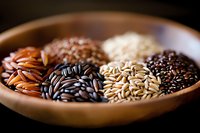Variety of raw rice grains in wooden bowl showing different colors and types including brown, black, white and wild rice. Close up with selective focus.