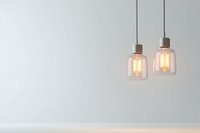 Modern pendant lights with glowing filament bulbs in glass shades hanging against white wall, creating minimal contemporary interior lighting atmosphere.