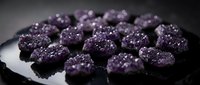 Gourmet purple chocolate truffles with sparkling sugar crystals arranged on elegant black plate for luxury dessert presentation and culinary photography.