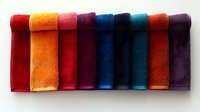 Colorful folded towels arranged in row showing vibrant spectrum from red through orange, pink, purple, blue and teal creating modern minimalist composition on white background.