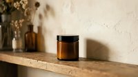 Amber glass jar with black lid on wooden shelf, natural skincare cosmetic container for cream or balm storage in minimalist bathroom setting.