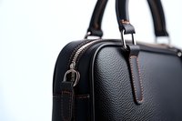 Close-up view of black leather handbag with orange contrast stitching showing textured surface, zipper detail and handle attachment on white background.