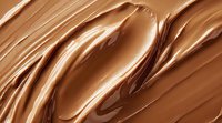 Smooth flowing chocolate cream texture with glossy swirls and waves creating luxurious abstract pattern in rich brown and caramel tones. Macro food background.