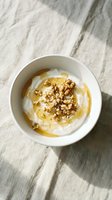 Greek yogurt with honey and walnuts in white bowl on marble surface. Healthy breakfast or snack option with natural ingredients for wellness lifestyle.