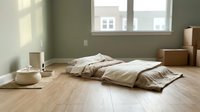 Minimalist bedroom interior with unmade bedding on wooden floor, natural light from window, neutral tones, and sparse furnishings for home design and lifestyle concepts.