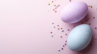 Pastel colored Easter eggs with tiny star confetti scattered on soft pink background. Minimal holiday composition with copy space for seasonal designs.