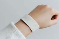 Wrist band mockup on pale skin tone arm wearing white sleeve, isolated on neutral background for branding and product design applications.