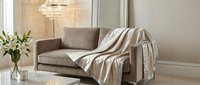 Cozy living room interior with modern beige sofa, striped throw blanket, fresh flowers in vase, and crystal chandelier for home decor design.