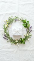 Natural herb wreath with lavender, rosemary, chamomile and mint surrounding white gift box on marble surface for spa wellness and aromatherapy concepts.