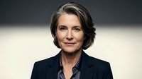Confident mature Caucasian businesswoman with gray hair in dark blazer, professional studio portrait with neutral background.