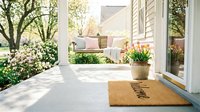 Cozy front porch with welcome doormat, swing, pink tulips, and blooming spring garden, evoking warmth and home comfort.