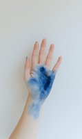 Open palm with blue paint or ink stain spreading across skin against white background for creative art and design projects.
