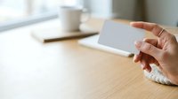 Woman holding blank white business card at wooden desk with coffee cup and notebook, suitable for corporate branding and professional networking materials.