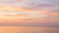 Serene seascape at sunset with soft pastel colors, calm ocean waters, and distant sailboat on horizon. Peaceful coastal scene for travel, wellness, and nature projects.