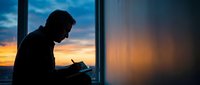 Silhouetted male professional working on laptop at window during sunset, ideal for business, technology, and remote work concepts.