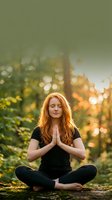 Young redhead woman meditating in lotus pose outdoors during golden hour sunset with hands in prayer position practicing mindfulness and yoga in nature.