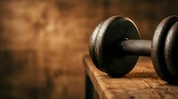 Old rusty dumbbell weight on wooden surface with warm brown background, suitable for fitness, gym, and strength training concepts.