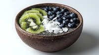 Fresh smoothie bowl with sliced kiwi, blueberries, coconut flakes and chia seeds in rustic ceramic bowl on light background. Healthy breakfast concept.