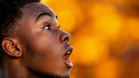 Young African American man with surprised expression looking up against vibrant orange background, profile view showing genuine emotion and wonder.