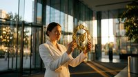 Professional businesswoman examining golden trophy award in modern corporate office building during sunset hour celebrating achievement and success.