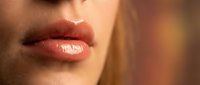 Close-up of woman's glossy coral lips with natural shine and smooth texture for beauty and cosmetics advertising campaigns.