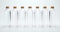 Seven clear glass bottles with cork stoppers arranged in row on white background for packaging design and product mockup presentations.