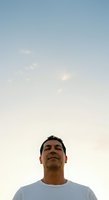 Middle-aged man with dark hair and olive complexion wearing light blue t-shirt gazes upward against serene pastel sky at dusk, conveying contemplation and hope for aspirational and motivational content.