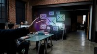 Digital communication technology, person interacting with holographic email icons floating in modern office workspace, virtual messaging interface.