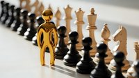 Golden metallic human figure standing prominently on chessboard among black and white chess pieces, symbolizing strategic leadership and business planning.