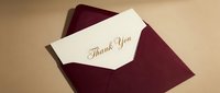 Elegant thank you card with gold script lettering tucked in a burgundy envelope on a beige background, perfect for gratitude and celebration concepts.