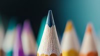 Sharp graphite pencil tip in macro view against blurred colorful pencils background, showcasing precision and creativity in art and education context.